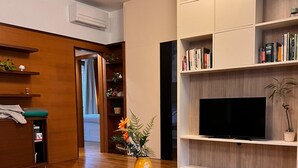 A modern living room with a wooden floor, a round coffee table with a vase of flowers, a sofa, a bookshelf, and a flat-screen TV. - 10 minutes from the Duomo LA TERRAZZA SU MILANO offers a moment of tranquility (Milano)