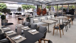 Un restaurante moderno con diversas opciones de asientos, incluyendo mesas y un área con sofás, con techo de cristal que permite la entrada de luz natural.