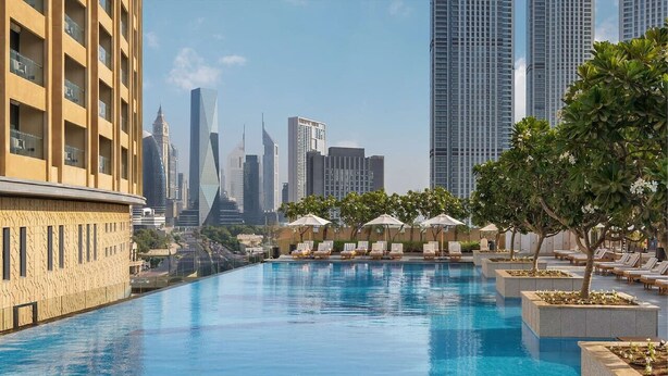 Piscina con sillas de descanso y macetas, rodeada de edificios altos.
