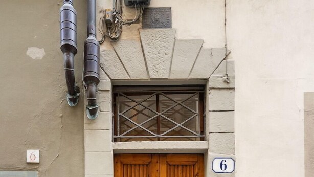 Puerta doble de madera con un pequeño ventanal arriba, un cartel con el número '6' y un timbre en la pared.