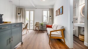Una sala de estar moderna con un sofá, una mesa de comedor y una zona de cocina con un lavamanos y armarios.
