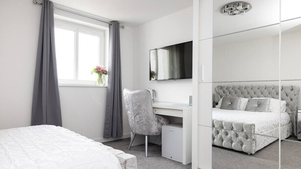 A bedroom with a bed, a desk, a chair, a mirror, and a window with curtains. - Elegant Flat with Balcony (Edinburgh)