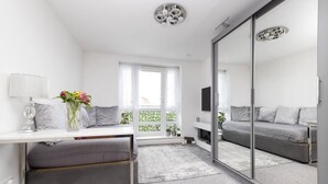 A modern bedroom with a large mirror, grey sofa, and a small table with a vase of flowers. - Elegant Flat with Balcony (Edinburgh)