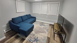 Un soggiorno con un divano angolare blu, un tappeto decorato, un tavolino in legno e un mobile porta TV.