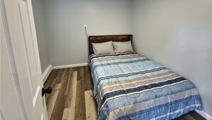 Una camera da letto con un letto, pavimento in legno e una porta.
