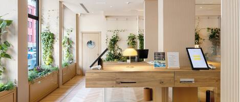 Un comptoir d’accueil moderne avec un revêtement en bois, des supports en verre transparent et une composition florale en pot.