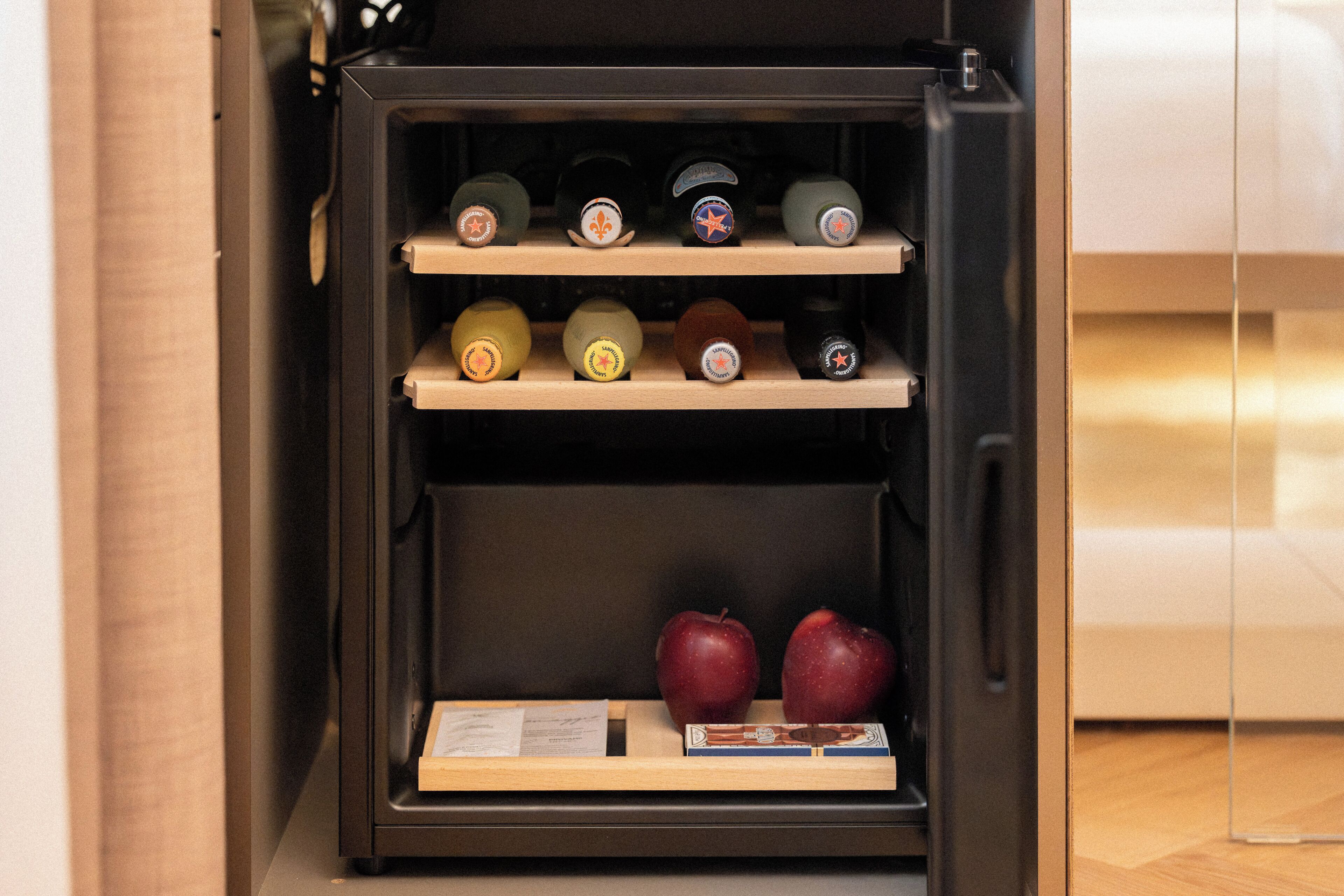 A wine refrigerator with multiple shelves, two apples, and a booklet.