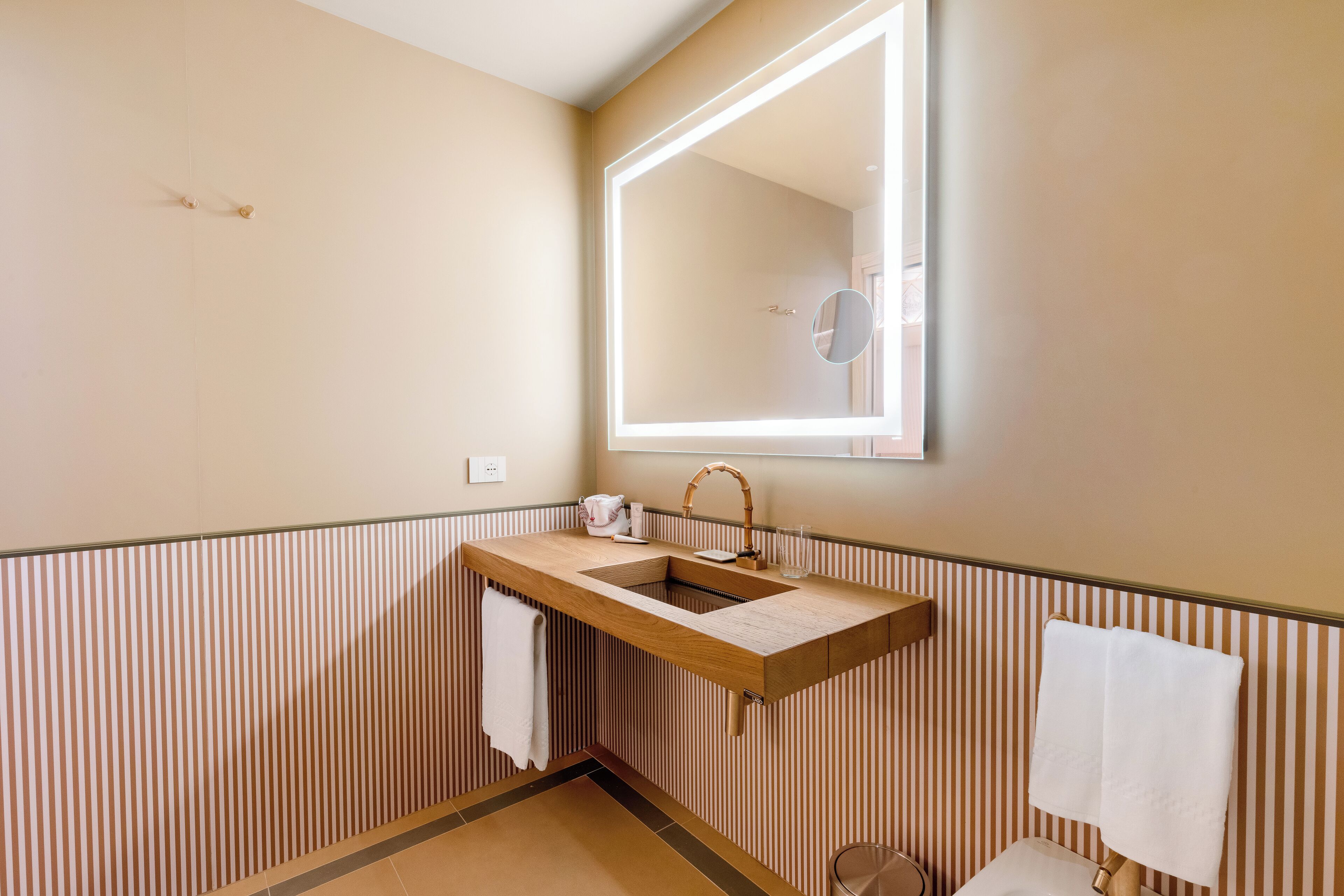 Un baño con tocador de madera, un espejo grande y papel tapiz a rayas.