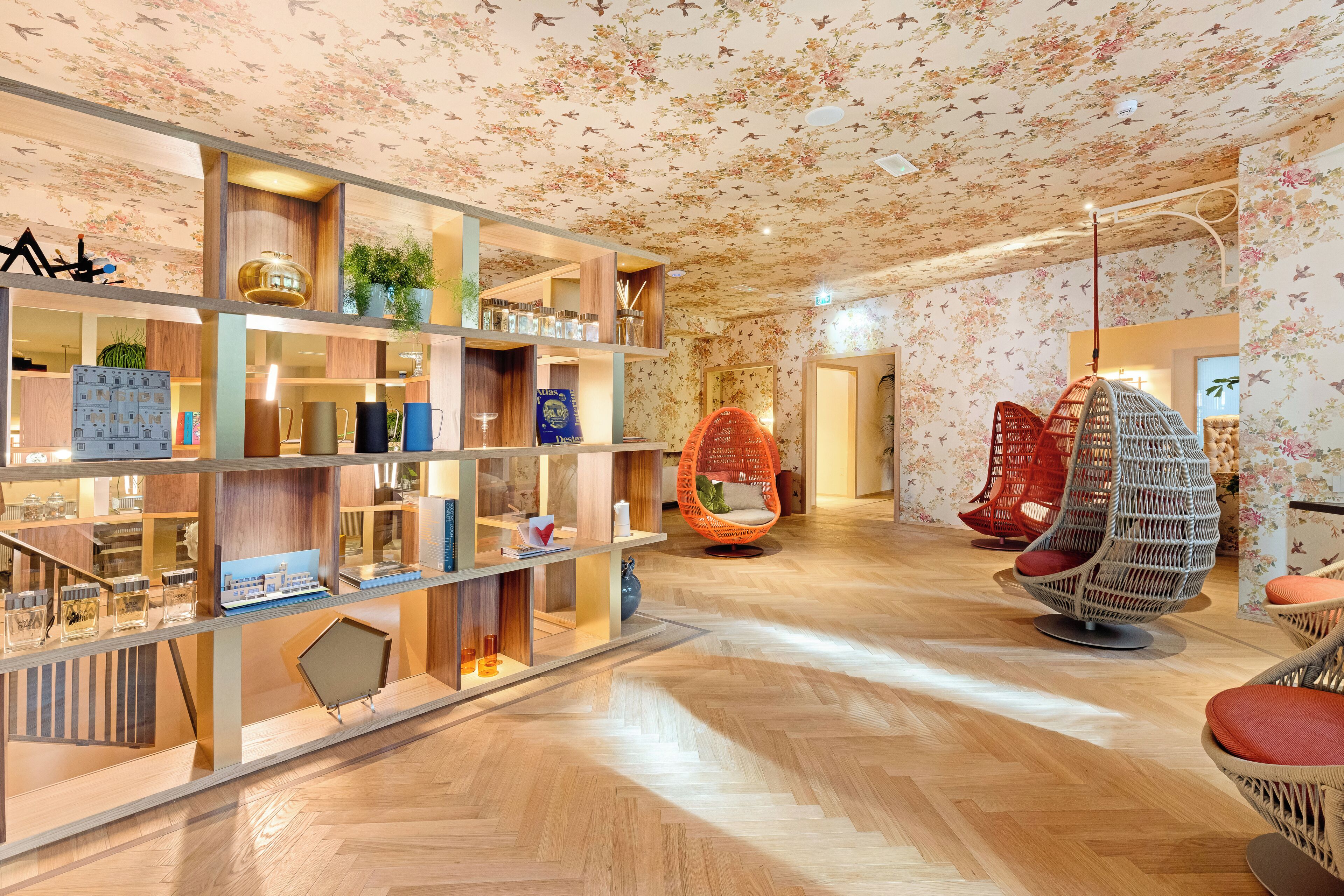 Een modern interieur met houten vloeren, een centraal wandmeubel met diverse objecten en kleurrijke hangstoelen.