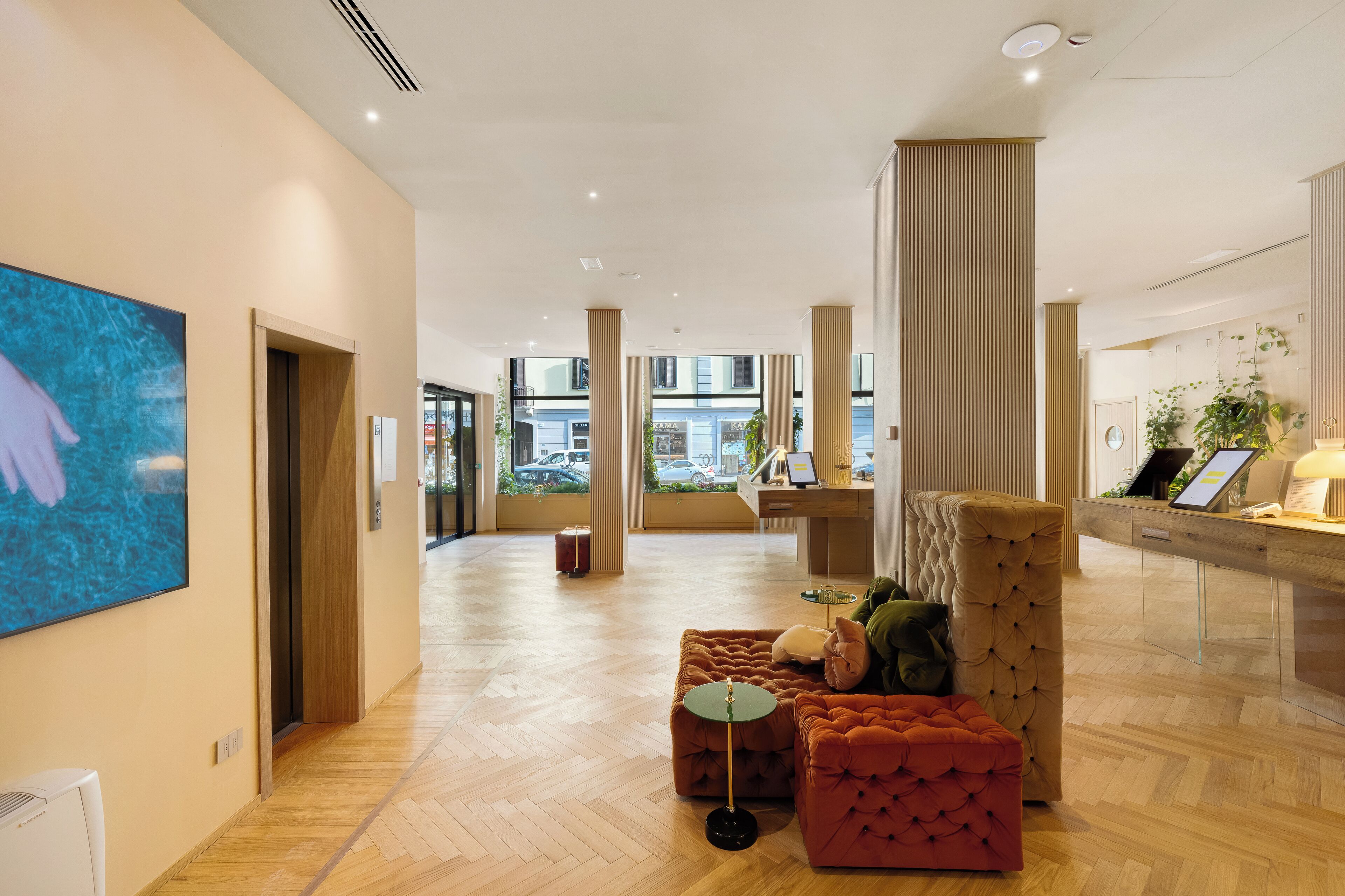 Un hall espacioso con suelo de madera, un mostrador de recepción y una zona de estar con un sillón y reposapiés capitonados.