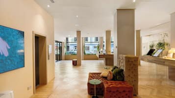 Un hall espacioso con suelo de madera, un mostrador de recepción y una zona de estar con un sillón y reposapiés capitonados.