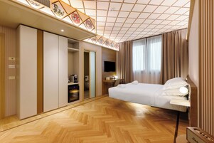 Una camera d'albergo con un letto, una scrivania con una lampada, una televisione e un armadio.