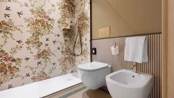 Casa de banho com chuveiro, sanita e lavatório, com papel de parede floral e painéis listrados.