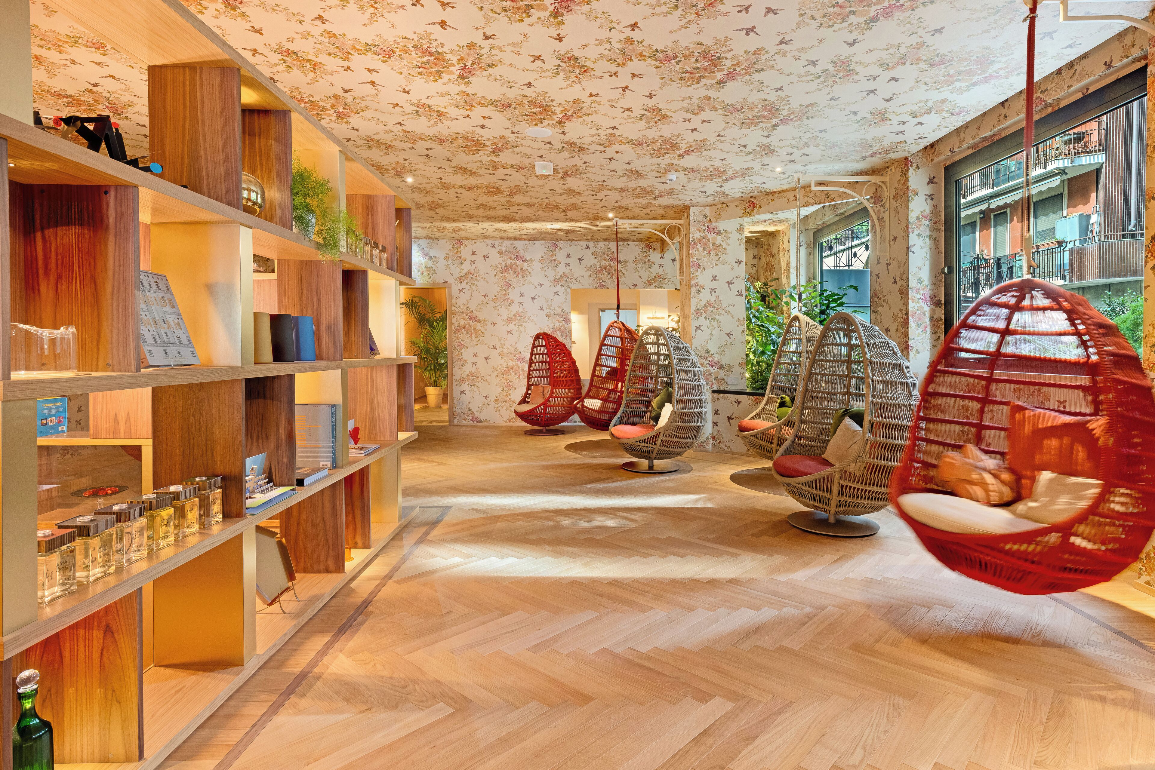 A hotel lobby with wooden shelves, hanging red chairs, and a floral ceiling.