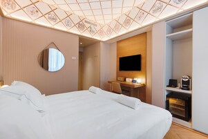 Camera d'albergo con un grande letto, una scrivania con una sedia, una TV a schermo piatto, una macchina del caffè e un minibar.
