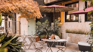 Un patio al aire libre con mesas, sillas, plantas en macetas y sombrillas.