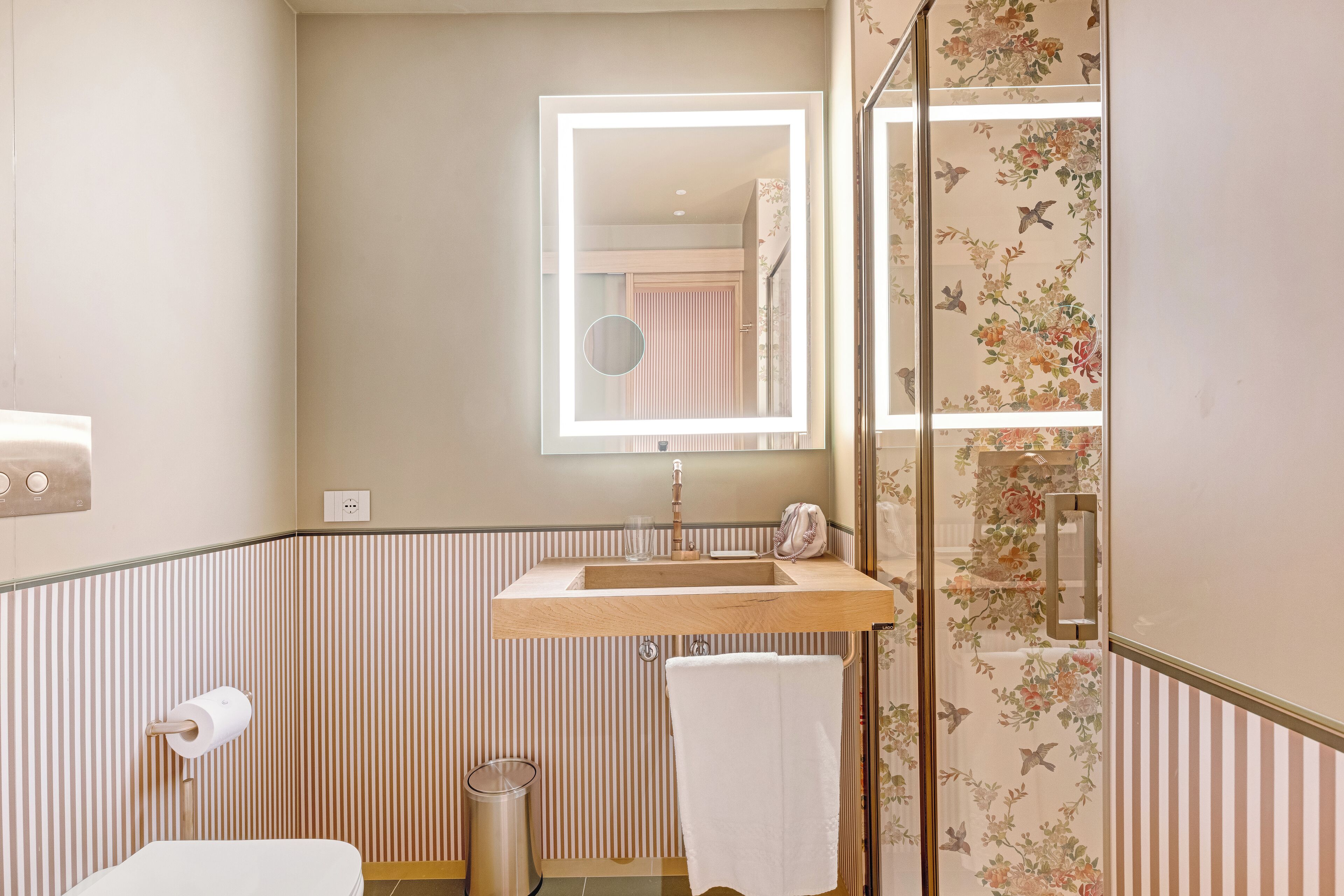 Un baño con tocador de madera, espejo, toalla y papel tapiz a rayas.