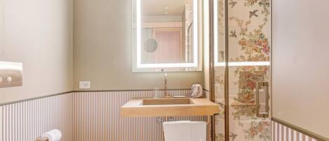 A bathroom with a wooden vanity, a mirror, a towel, and striped wallpaper.