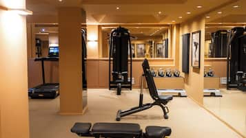 Un gimnasio con equipo de ejercicio, cinta de correr y pared espejada.