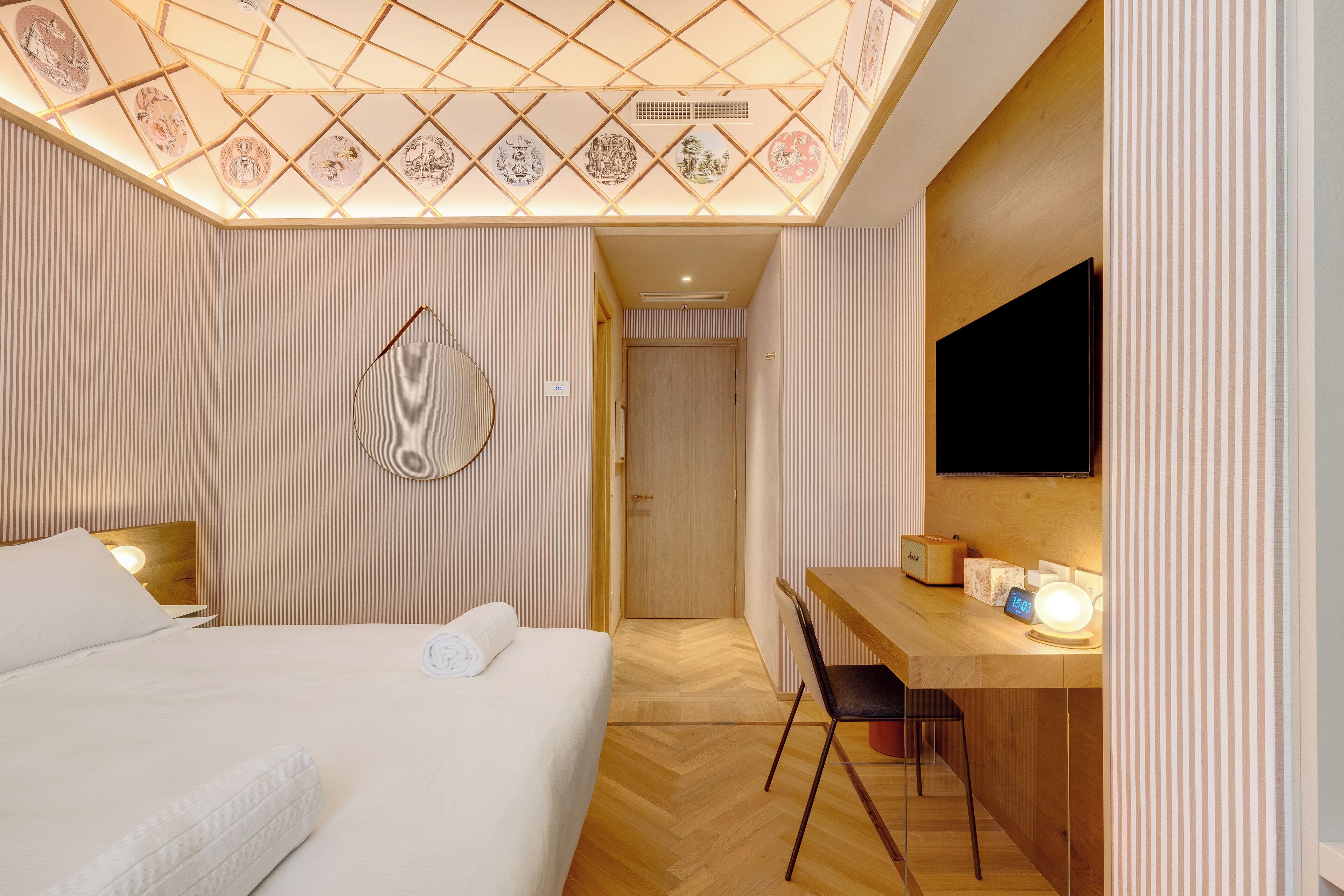 Ein Hotelzimmer mit Bett, Schreibtisch, Stuhl, Fernseher und Decke mit gemusterten Fliesen.
