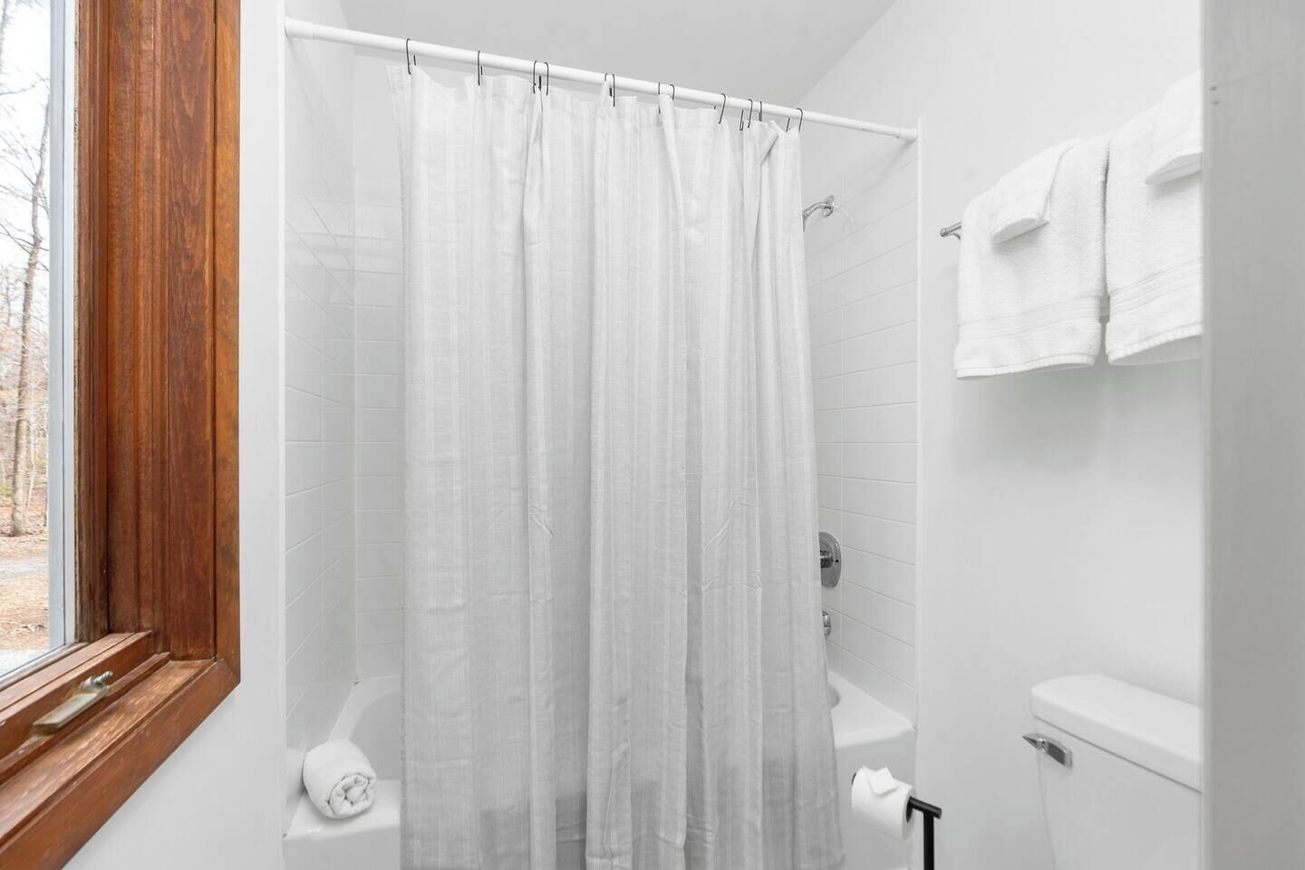 A bathroom with a shower curtain, a toilet, and a window with a wooden frame.