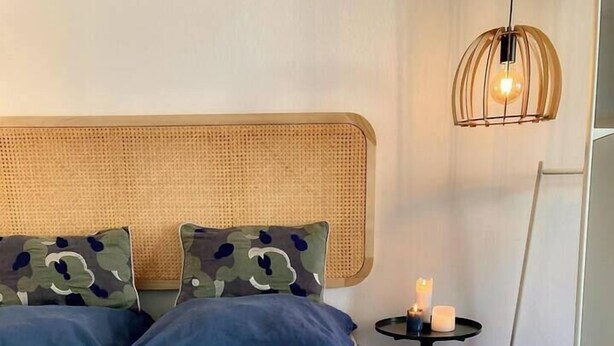 Un lit bien fait, avec une literie bleue et beige, une tête de lit en rotin et une petite table de chevet ornée de bougies.