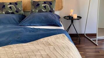 Ein ordentlich bezogenes Bett mit blau-beiger Bettwäsche, einem Rattan-Kopfschild und einem kleinen Nachttisch mit Kerzen.