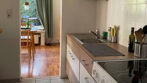 Une cuisine compacte équipée d’une cuisinière, d’un four et de placards. On aperçoit un coin repas à travers une porte ouverte.