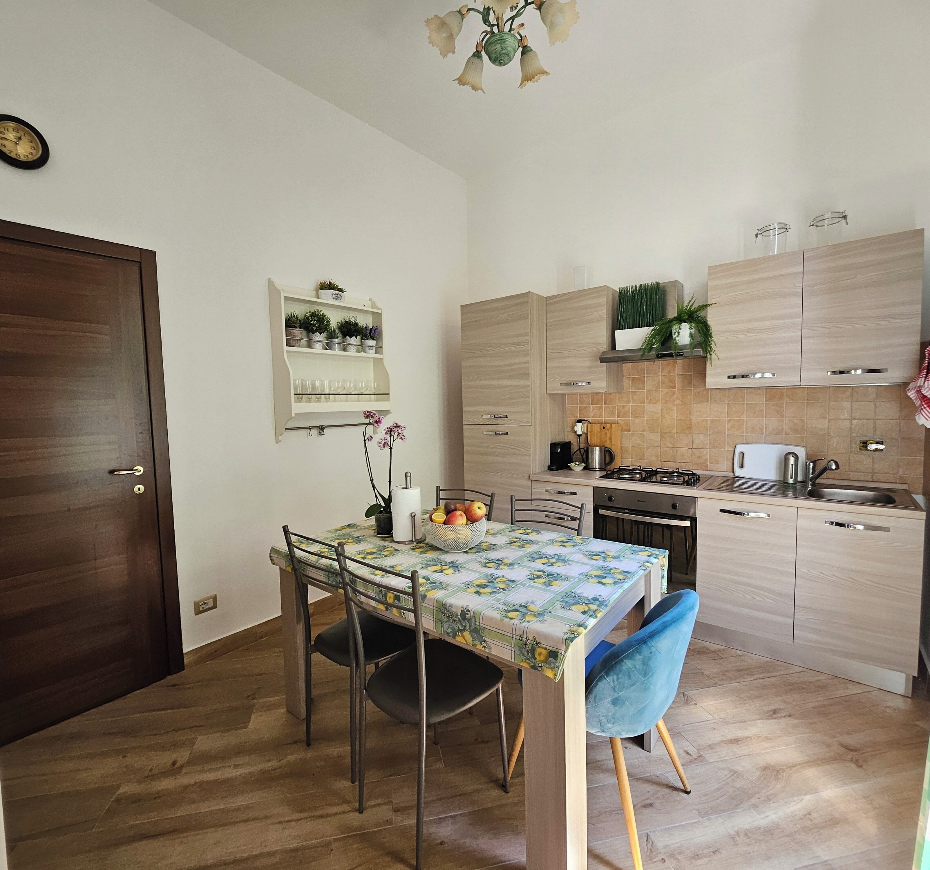Eine kleine Küche mit Holzausstattung, einem Esstisch mit Stühlen und einer Arbeitsfläche mit Wasserkocher und Toaster.