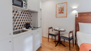 Uma cozinha compacta com micro-ondas, torradeira e máquina de café. Existe um pequeno espaço de jantar com duas cadeiras e uma mesa posta para dois. Uma obra de arte emoldurada está pendurada na parede acima da área de jantar.
