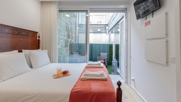 Quarto de hotel com uma cama, uma televisão na parede e vista para a área externa.