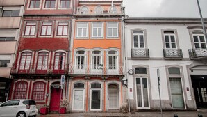 Uma fileira de edifícios altos com estilos arquitetônicos variados, incluindo fachada de tijolos vermelhos, um edifício laranja com janelas brancas e um edifício branco com sacadas.