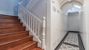 Uma escadaria de madeira com balaústres brancos que leva a um patamar com piso estampado.