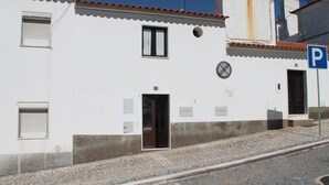 A white building with a tiled roof, a door, and a window with a curtain. - Casa dos Avós - Two Bedroom House, Sleeps 4 (Évora Monte)