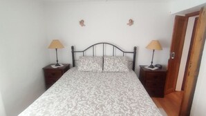 A single bed with a patterned bedspread, two bedside tables with lamps, and a wooden door. - Casa dos Avós - Two Bedroom House, Sleeps 4 (Évora Monte)