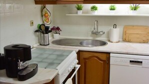 A compact kitchen with wooden cabinets, a white countertop, a sink, a coffee maker, and a dishwasher. - Casa dos Avós - Two Bedroom House, Sleeps 4 (Évora Monte)