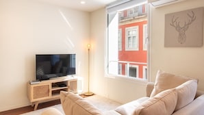 A living room with a TV, a floor lamp, and a window with a view of a red building. - Bombarda Cozy Studio by LovelyStay (Porto)