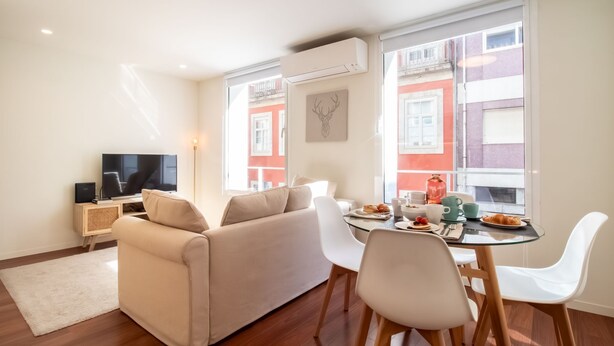 A modern living room with a sofa, a TV, and a dining area with a table set for breakfast. - Bombarda Cozy Studio by LovelyStay (Porto)