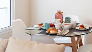 A breakfast setting with a glass table, white chairs, and a variety of breakfast items including pancakes, croissants, and fruit. - Bombarda Cozy Studio by LovelyStay (Porto)