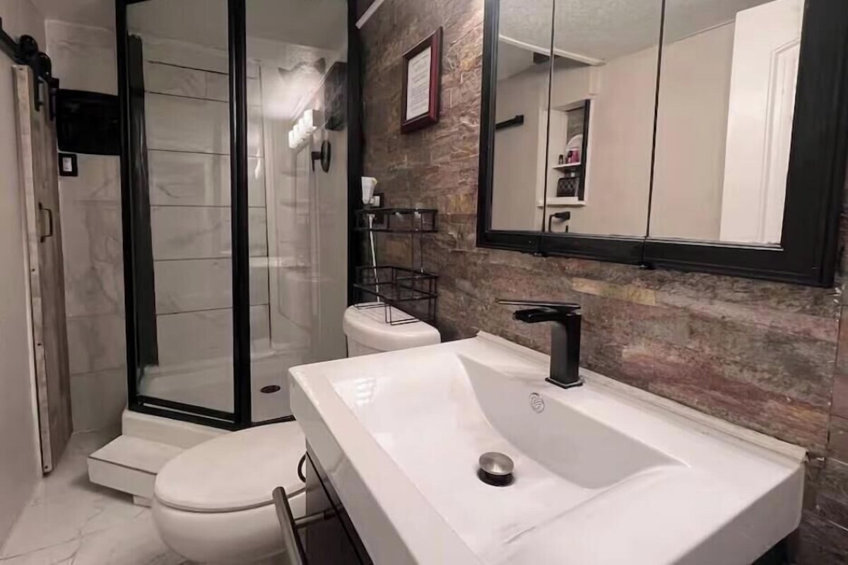 Un baño con ducha acristalada, lavamanos blanco y un espejo grande.