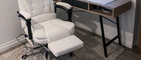 A modern office chair, a desk with a lamp, and a cityscape painting on the wall.