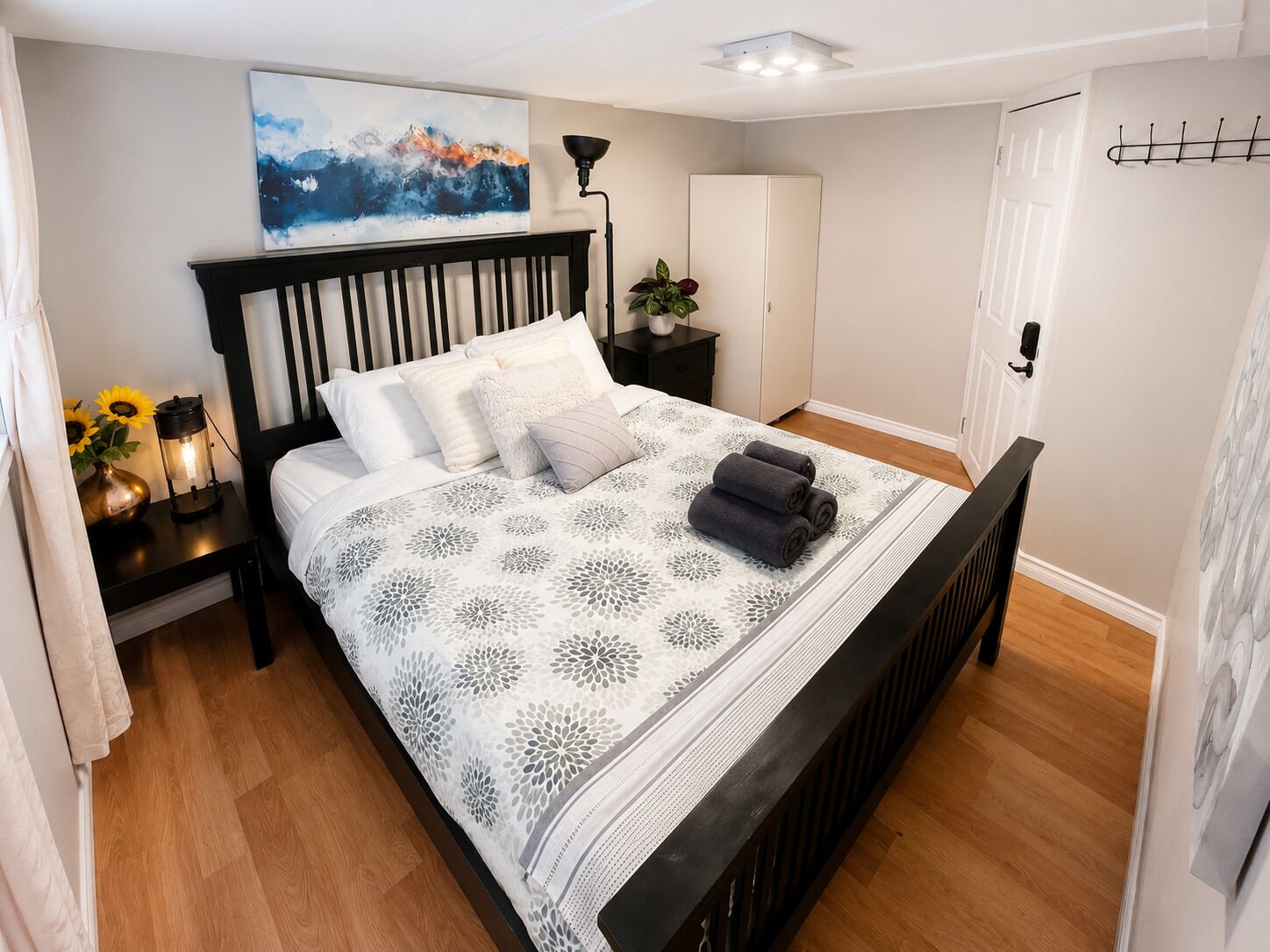 Un dormitorio con cama, mesita de noche, lámpara y un cuadro en la pared.