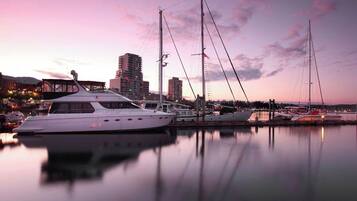 A marina with multiple yachts docked, a bridge in the background, and buildings along the waterfront.