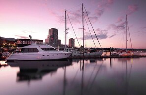 Ein Yachthafen mit mehreren dort angestuften Yachten, eine Brücke im Hintergrund und Gebäude entlang der Uferpromenade.