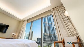 A hotel room with a bed, a TV, a desk, and a large window offering a city view.