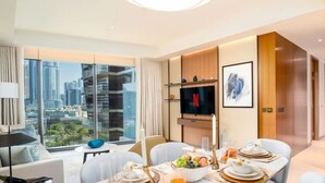 A modern hotel room with a dining area set for breakfast, a flat-screen TV, and a city view.