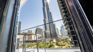 A balcony with a view of a tall skyscraper, a chair, and a table.