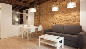 A modern living space with a stone wall, a white sofa, a dining table with chairs, and pendant lighting. - Habitat Apartments Alissia (Barcelona)