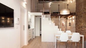 A modern kitchen with a built-in washing machine, a dining area with white chairs, and a stone wall. - Habitat Apartments Alissia (Barcelona)