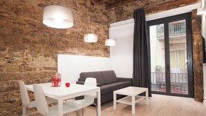 A modern living space with a stone wall, a white sofa, a dining table with chairs, and a balcony with a view. - Habitat Apartments Alissia (Barcelona)